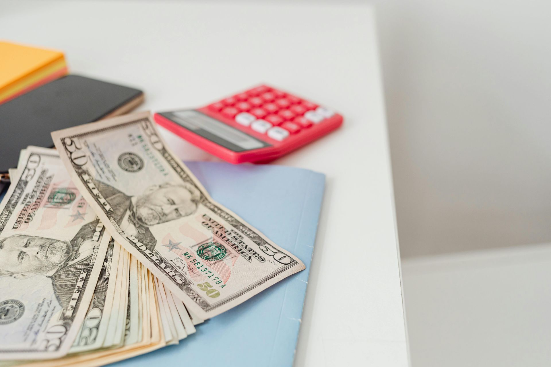 A pile of money is sitting on a table next to a calculator.