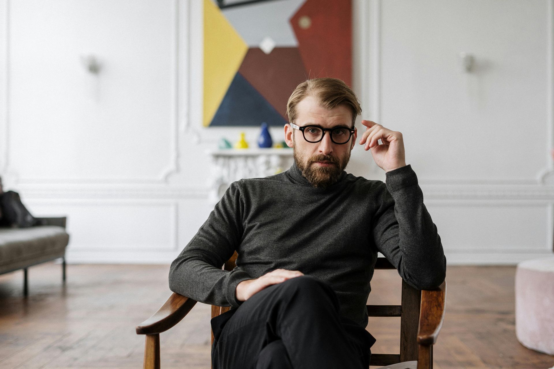 A man with glasses is sitting in a chair in a living room.