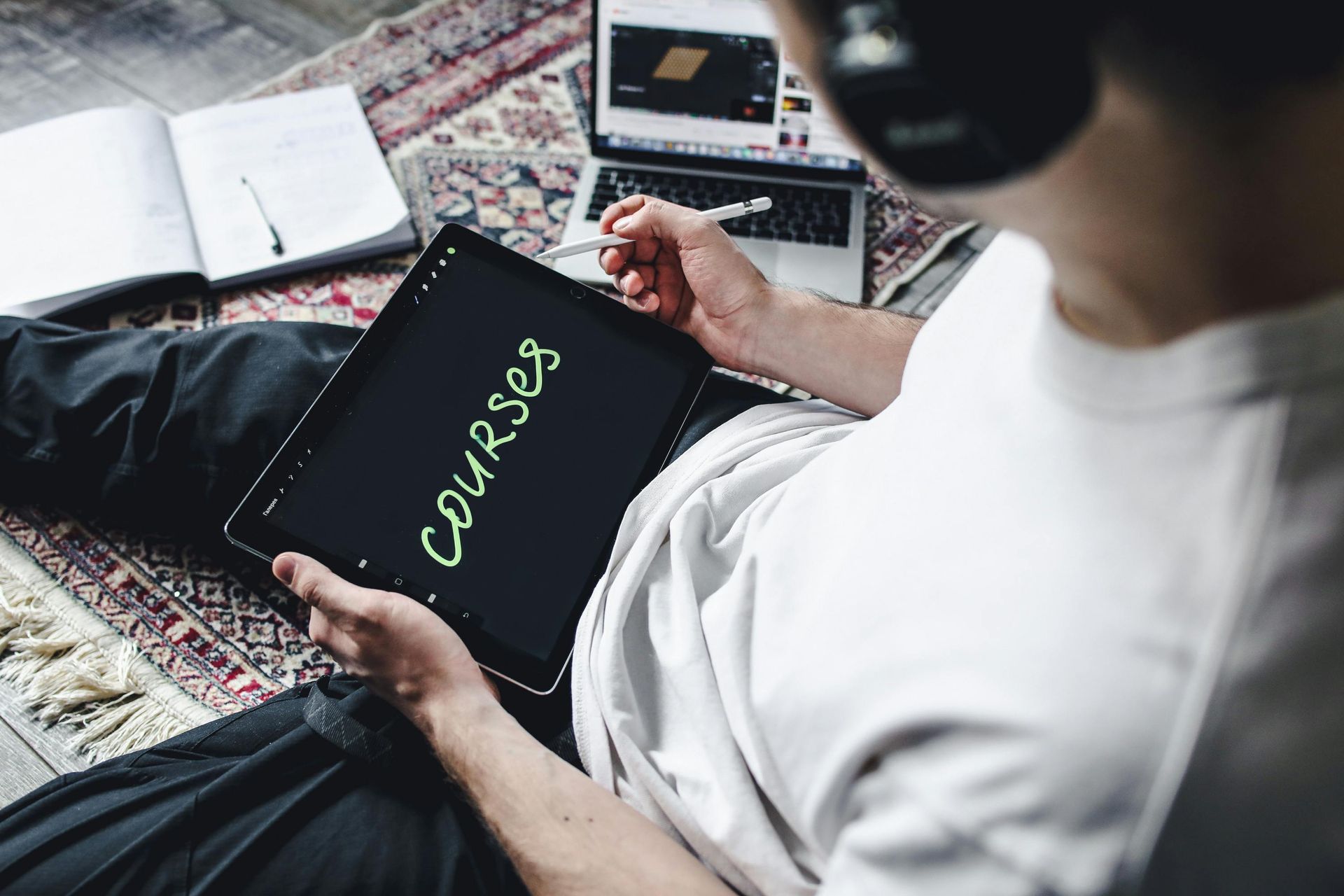 A man is sitting on the floor using a tablet with the word courses written on it.