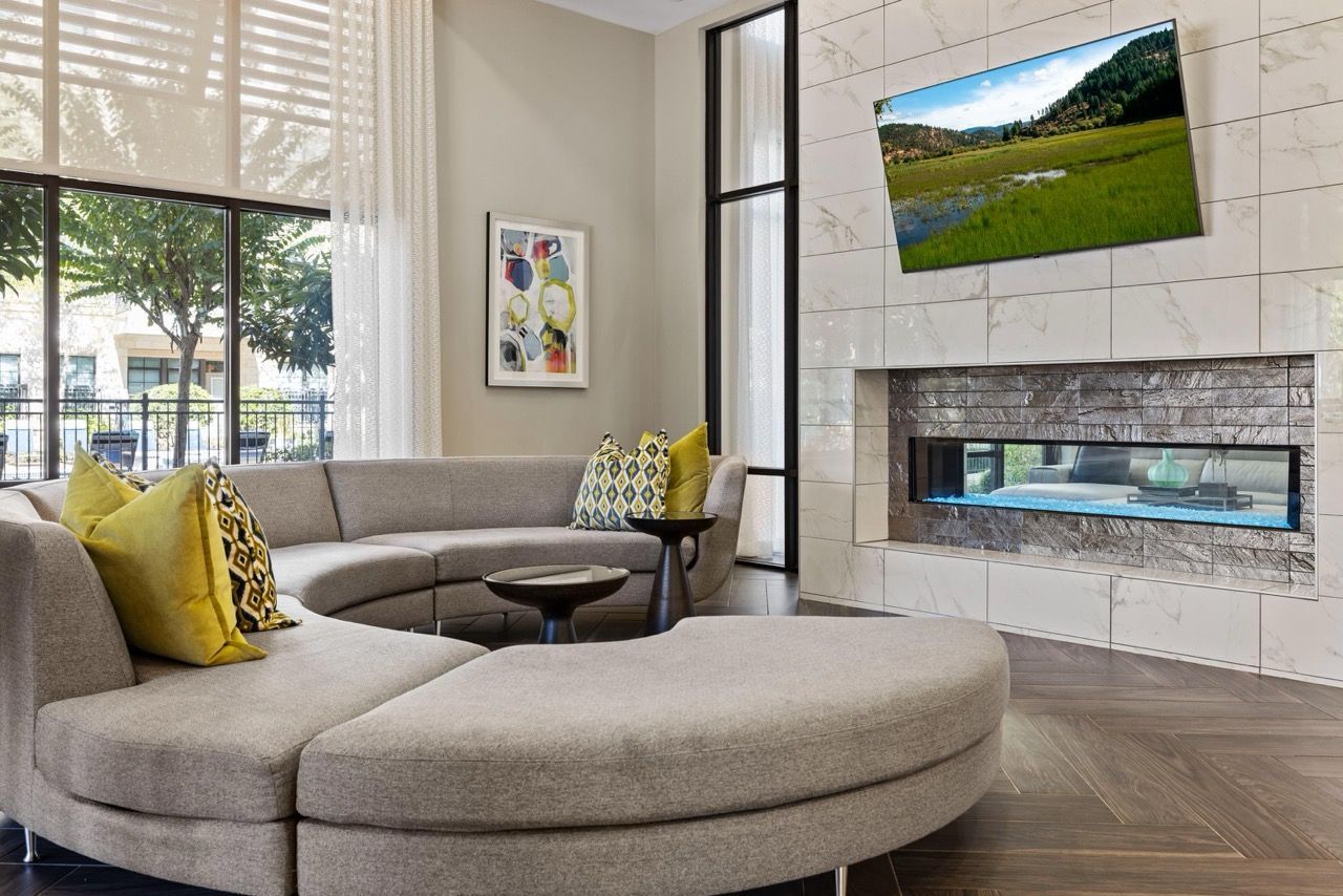 Modern apartment living room with curved beige sectional, marble-surround fireplace, and wall-mounted TV.