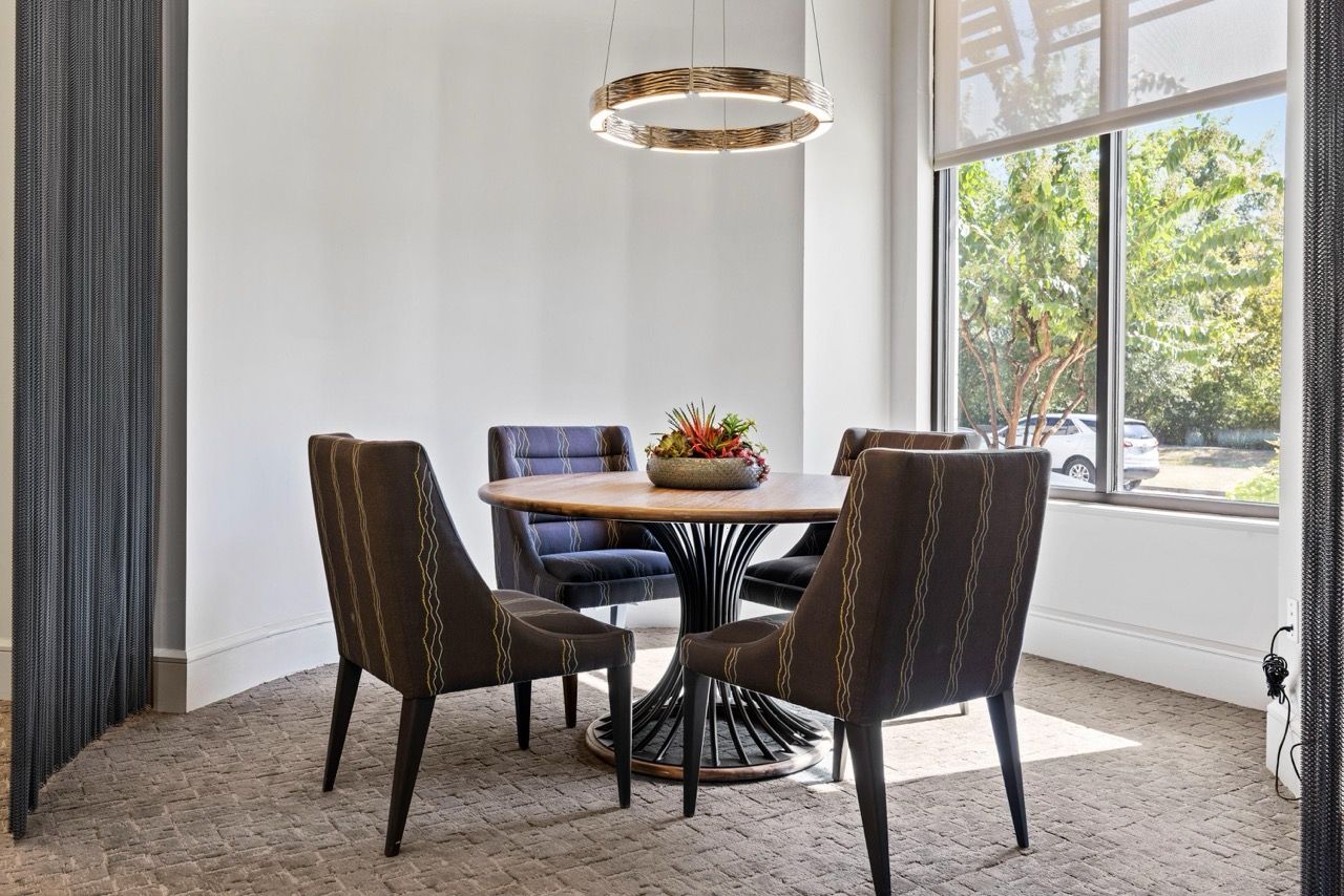 Dining area with a round wooden table and four striped upholstered chairs by a large window.