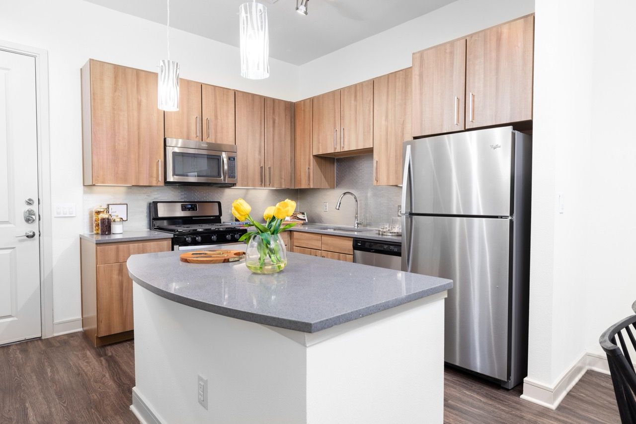 Modern kitchen with wooden cabinets, stainless steel appliances, island, and pendant lights.