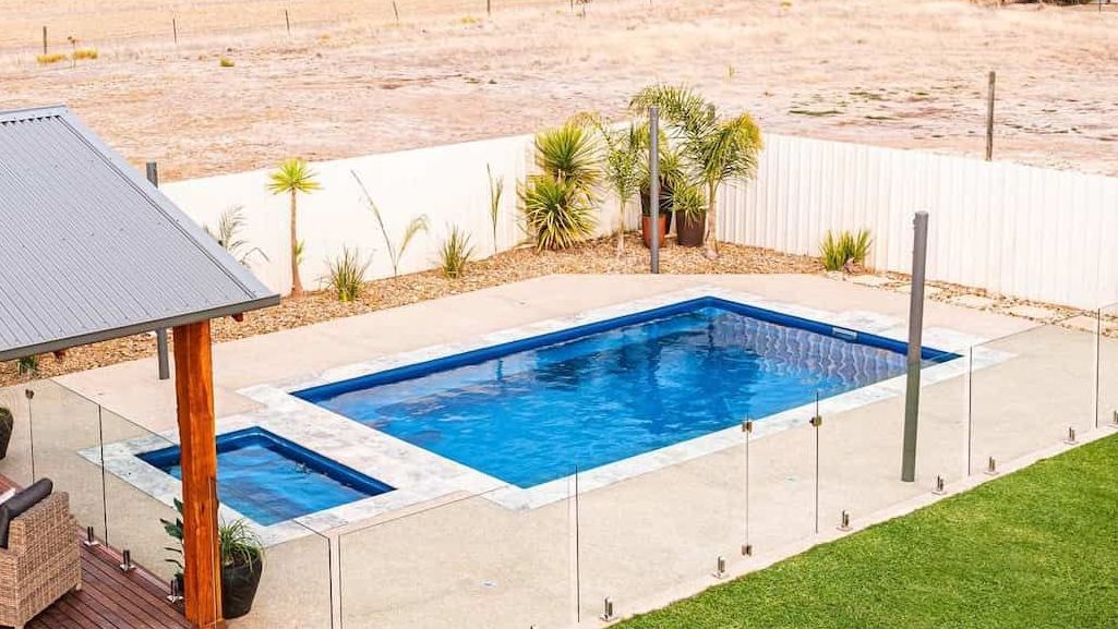A Large Swimming Pool Surrounded by a Glass Fence in a Backyard — Pooltech NT In Alawa, NT