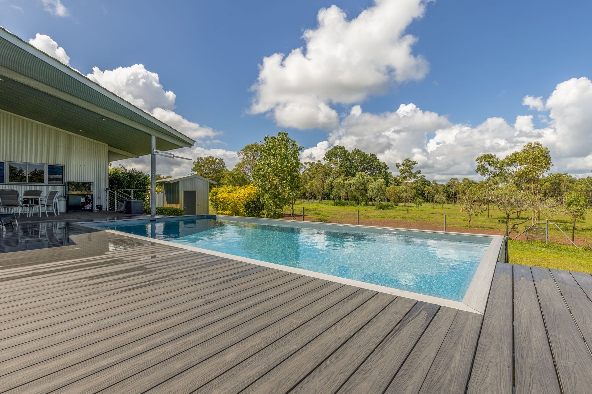 A Large Swimming Pool Is Surrounded by A Wooden Deck in Front of A House — Pooltech NT In Alawa, NT