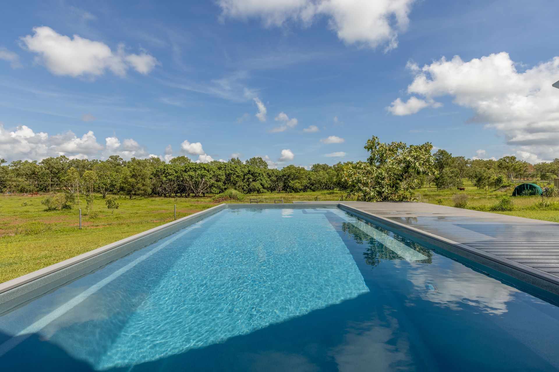 A Large Swimming Pool Surrounded by Grass and Trees on A Sunny Day — Pooltech NT In Alawa, NT