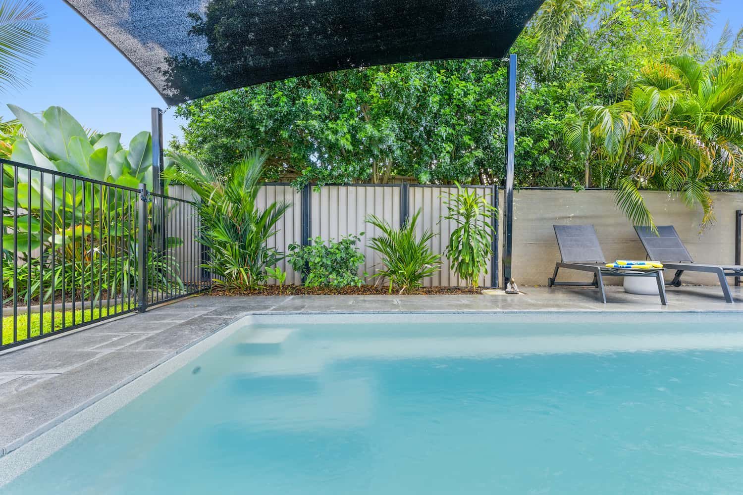 A Large Swimming Pool Surrounded by a Fence and Chairs Under an Umbrella — Pooltech NT In Alawa, NT