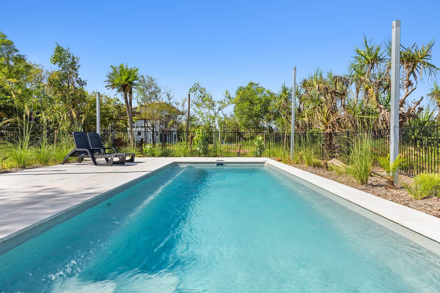 A Large Swimming Pool Surrounded by Trees and Chairs on a Sunny Day — Pooltech NT In Alawa, NT