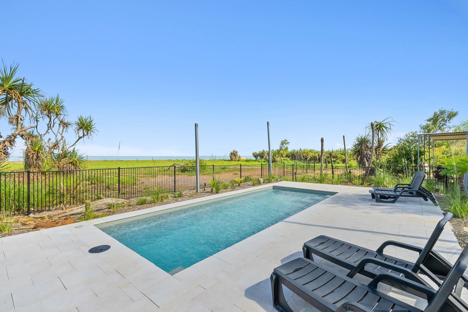A Large Swimming Pool Surrounded by Chairs and a Fence With a View of the Ocean — Pooltech NT In Alawa, NT