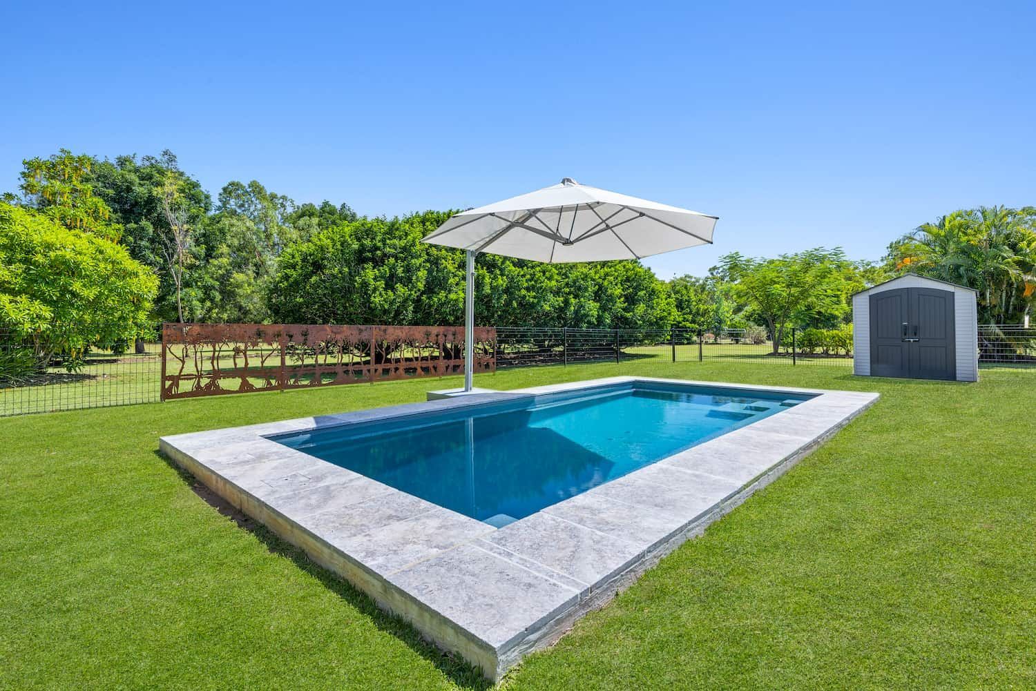 A Swimming Pool With an Umbrella and a Shed in the Background — Pooltech NT In Alawa, NT