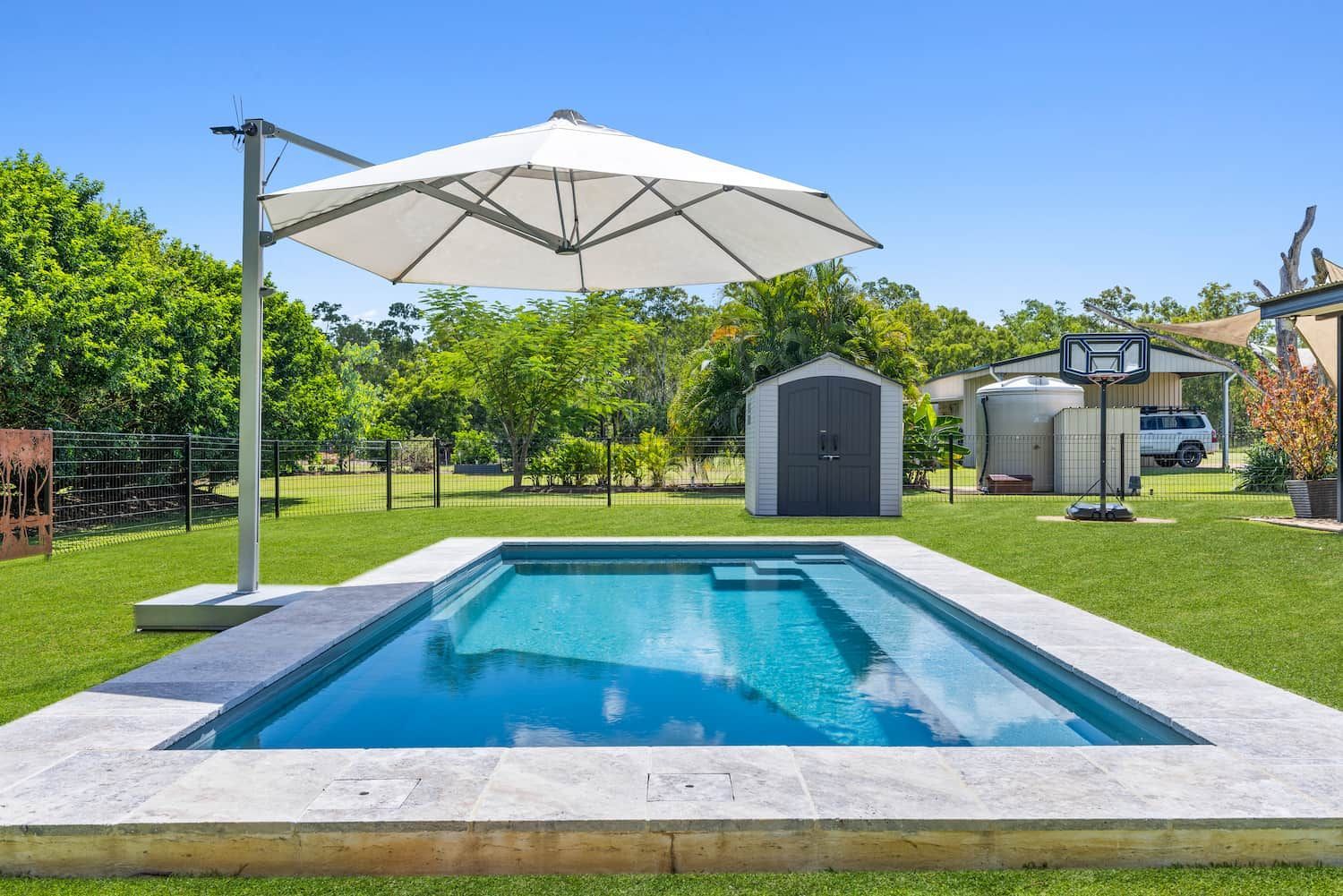 A Large Umbrella is Sitting Next to a Swimming Pool in a Backyard — Pooltech NT In Alawa, NT