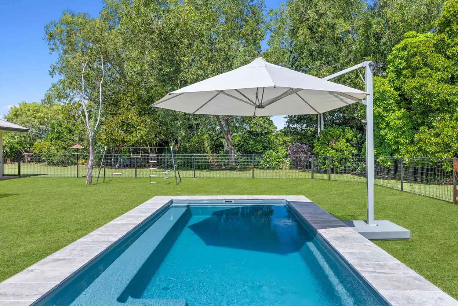 A Large Swimming Pool With a White Umbrella in Front of a House — Pooltech NT In Alawa, NT