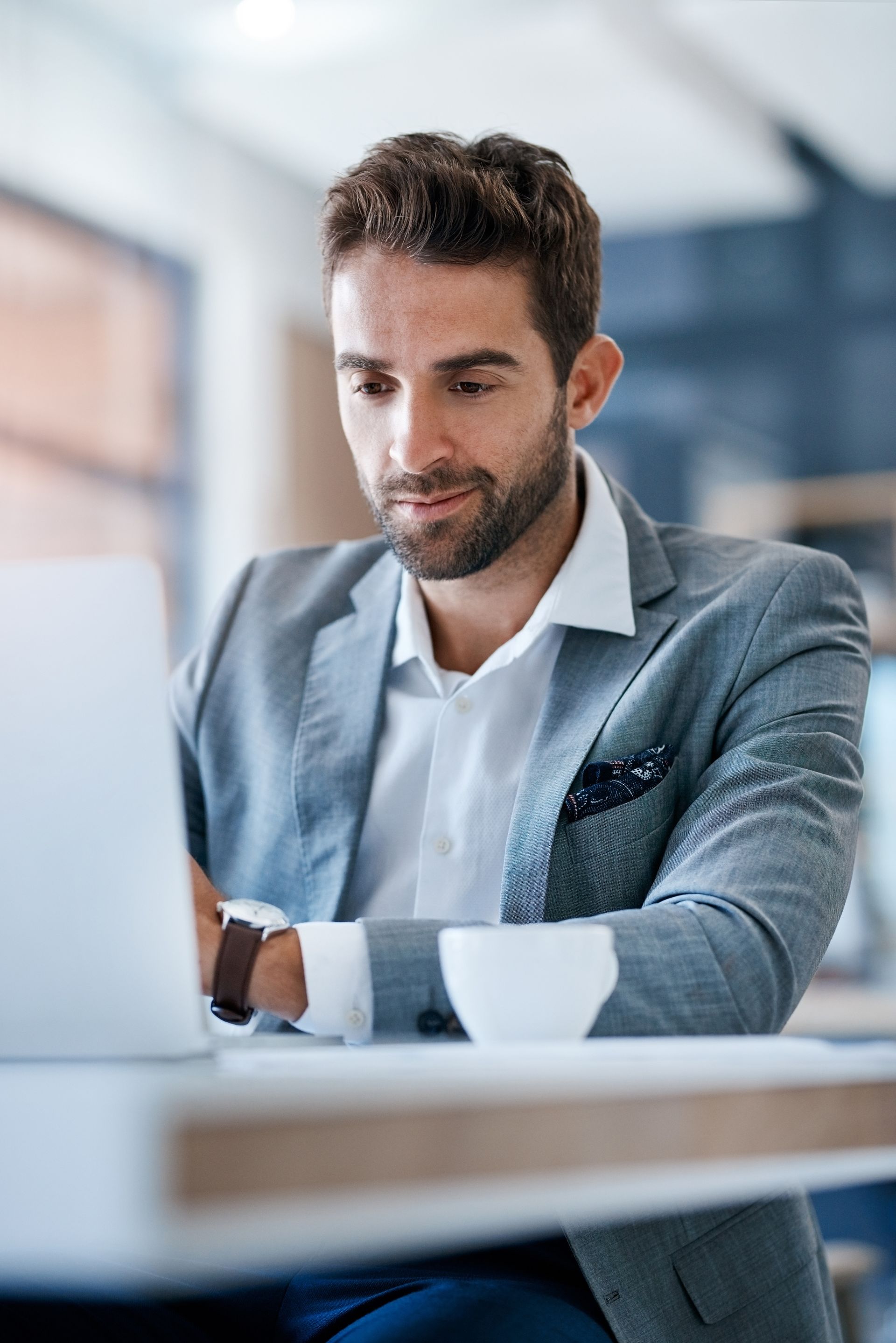 Man in gray blazer working on laptop in a cafe, looking intently.