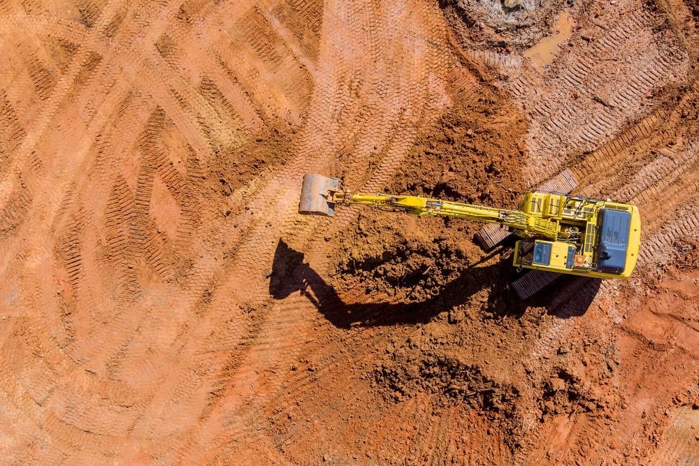 Yellow excavator digging in reddish-brown dirt at a construction site, top-down view — BC Earthmoving & Civil Construction in East Barron QLD