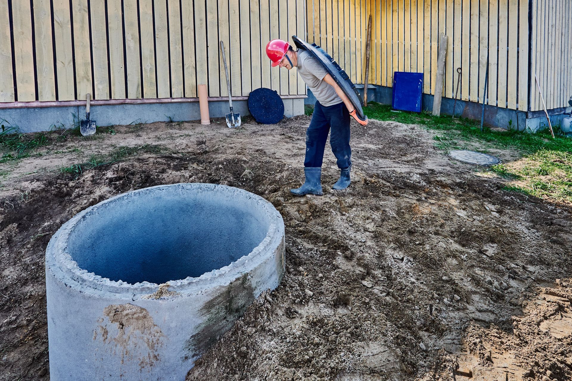 Person in Red Helmet Looking Into a Concrete Well Ring in a Yard — BC Earthmoving & Civil Construction in East Barron QLD
