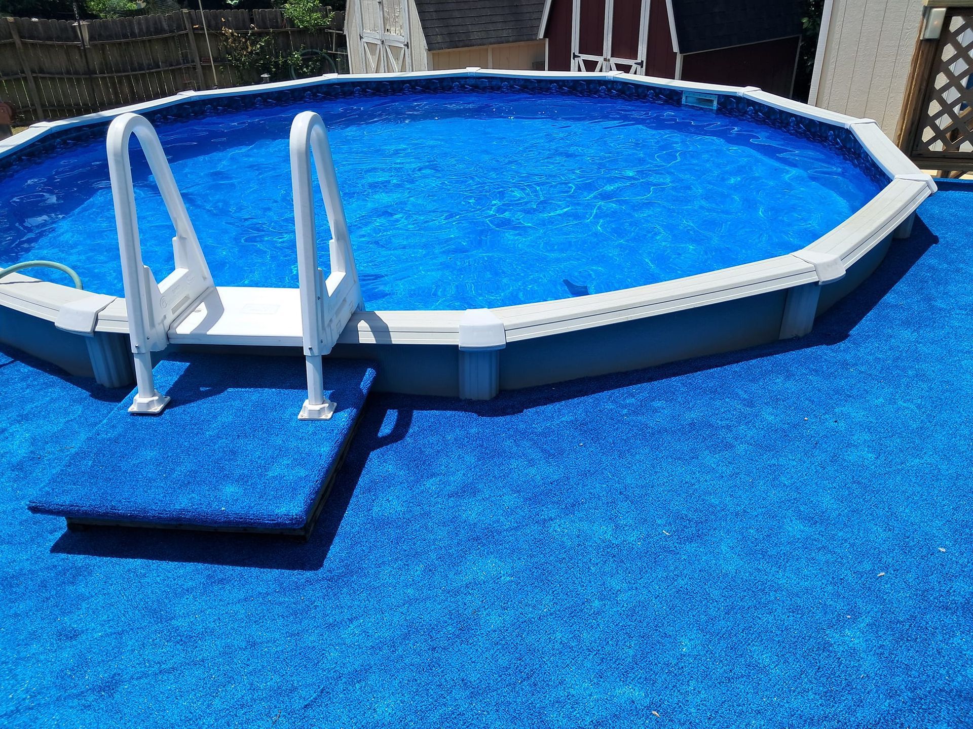 Above-ground round swimming pool with a white ladder and a blue-carpeted platform, set on a blue-surfaced deck.