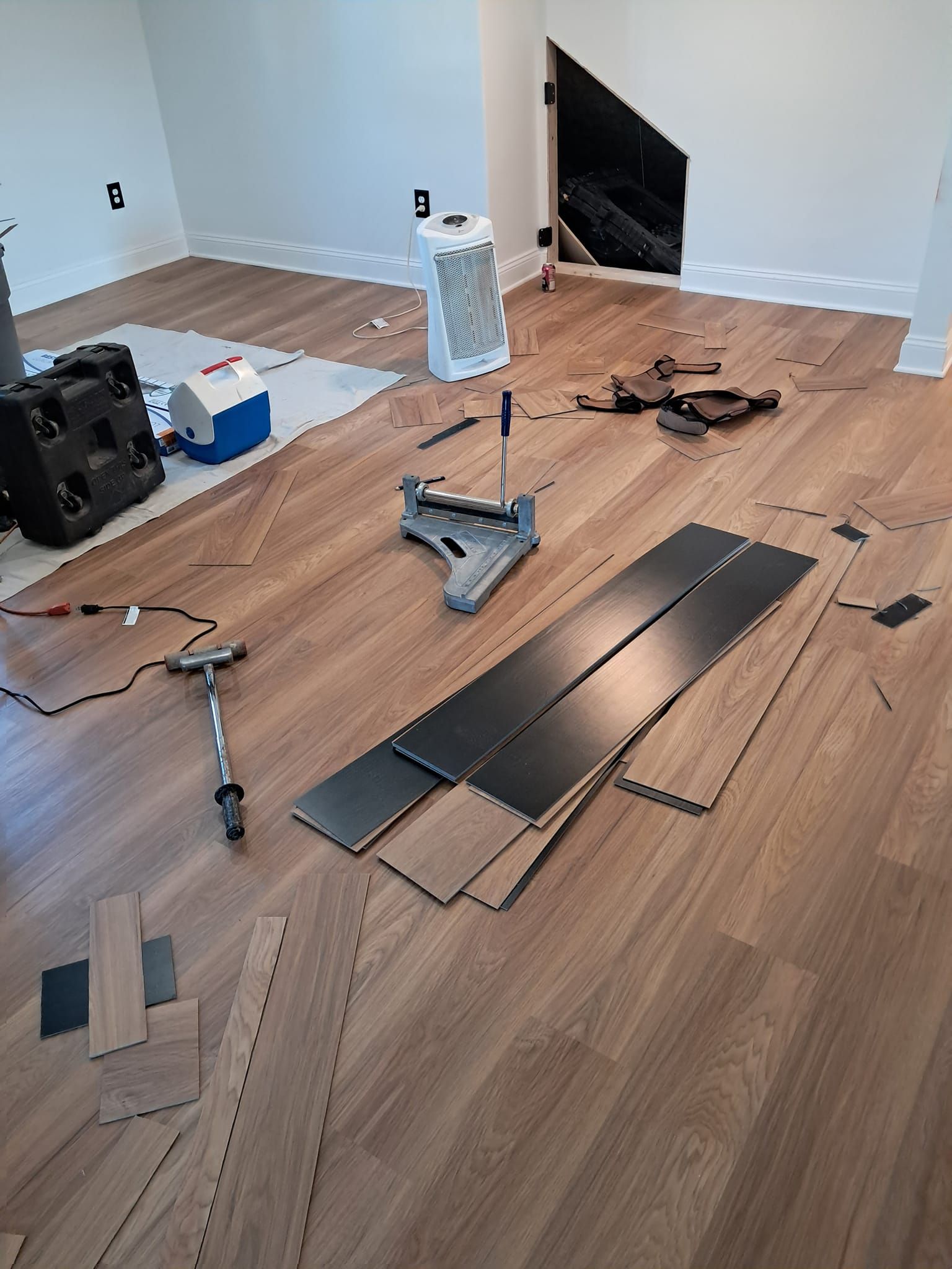 A room during a flooring renovation with wood-look planks, a cutting tool, and a mallet scattered on the finished floor.