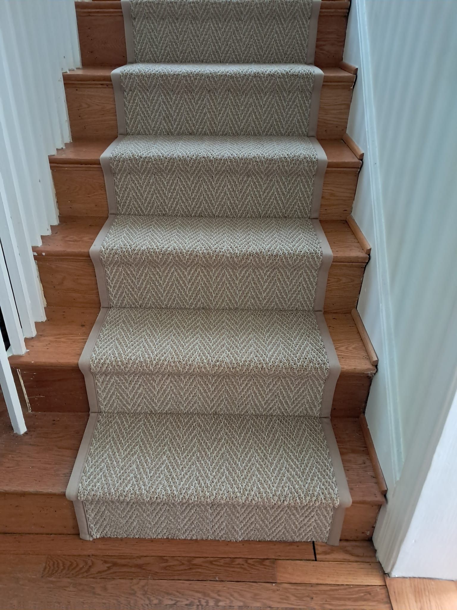 A staircase with wooden steps featuring a central beige, herringbone-patterned carpet runner.