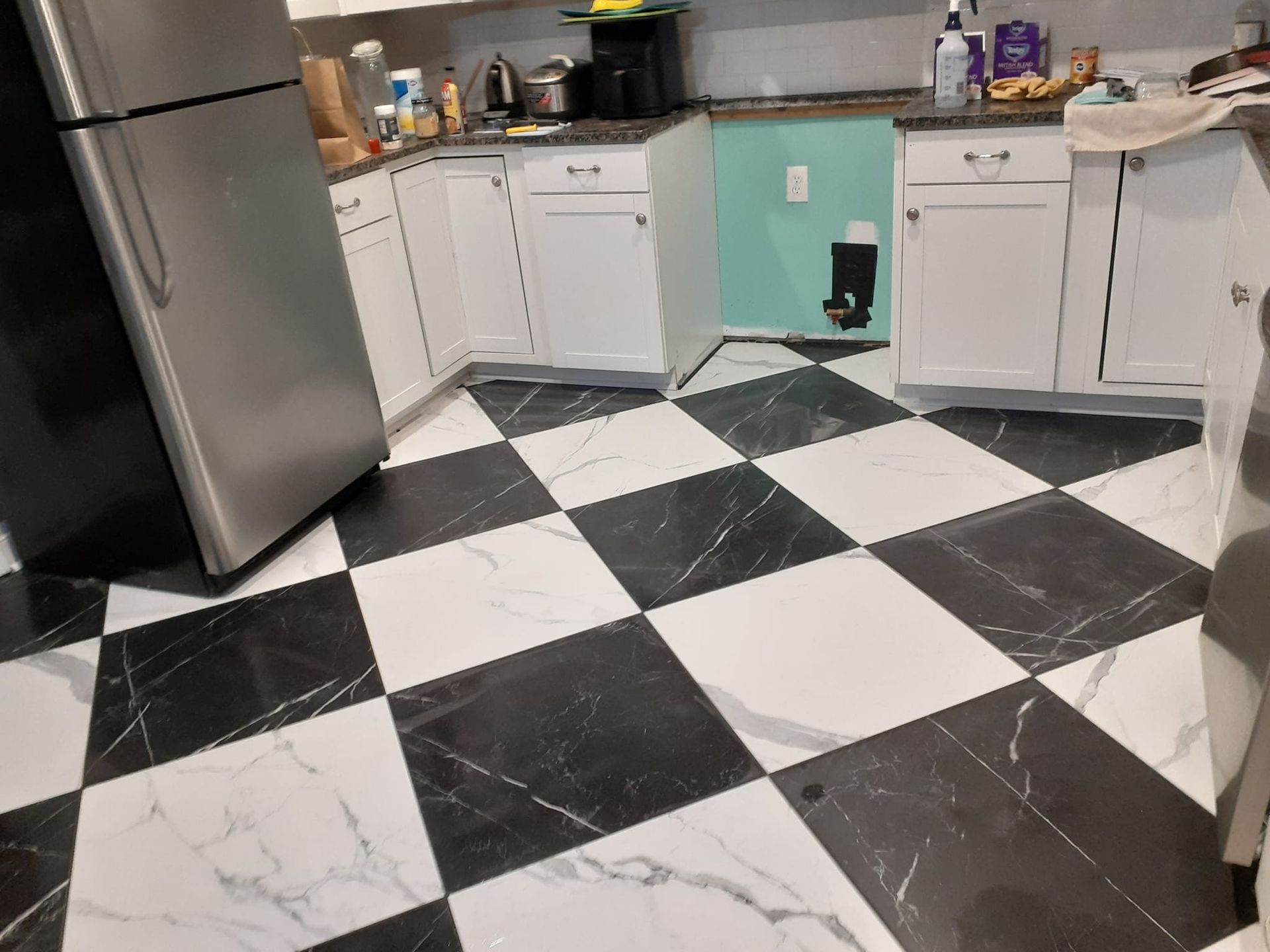 A kitchen with white cabinets, a stainless steel refrigerator, and a black-and-white marble checkered floor.