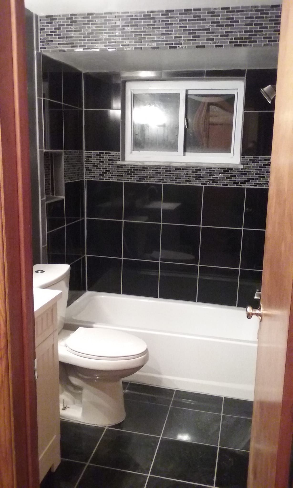 Two workers spread black mulch near a large decorative boulder on a landscaped residential property.