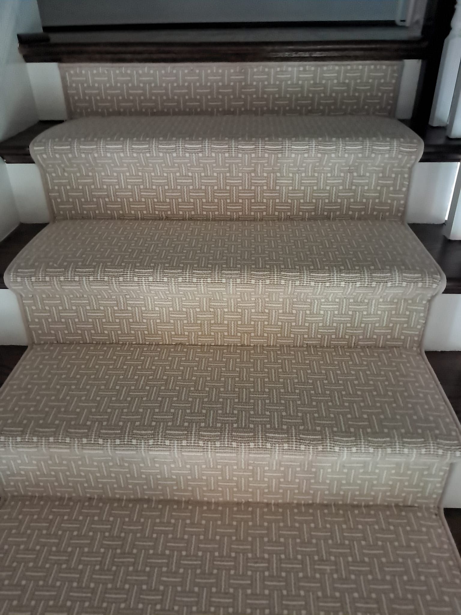 Stairs featuring a tan and white geometric patterned carpet runner over dark wood treads and white risers.