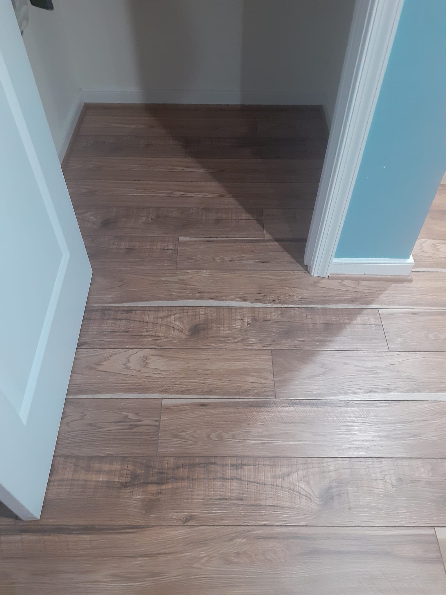 Buckled, light-brown wood-look flooring near a white door frame and a light blue wall.