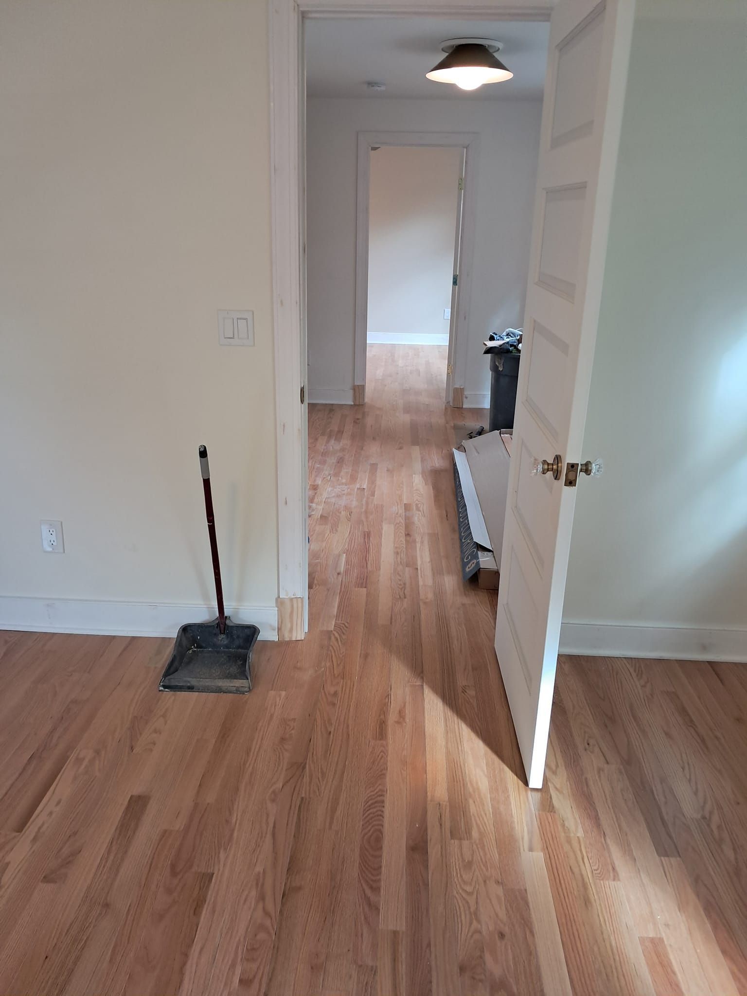 Light-toned hardwood floors extend from a room through an open white door into a hallway with another open doorway.