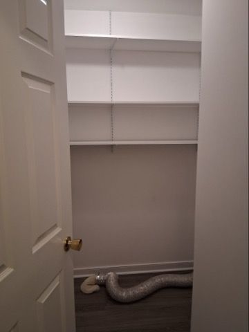 A small, empty closet with white shelves and a flexible silver dryer vent hose lying on the dark floor.