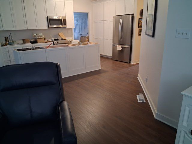 A dark blue leather armchair in the foreground faces a bright, open-plan kitchen with white cabinetry and wood flooring.
