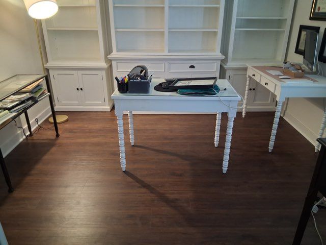 A bright home office with dark wood floors, white wooden desks, and white shelving units.
