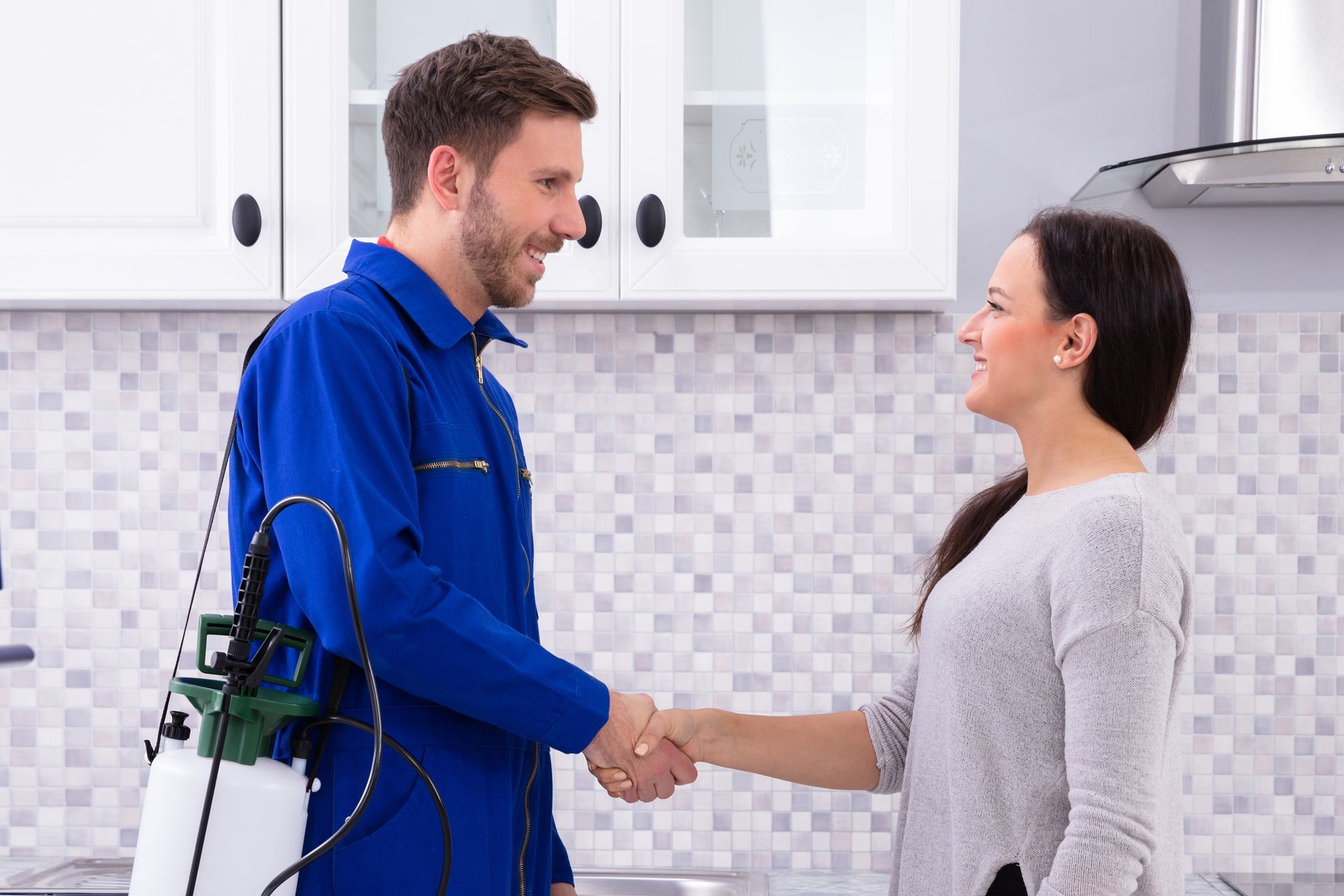 An exterminator from a pest control company, in a blue uniform, shaking hands with a woman.