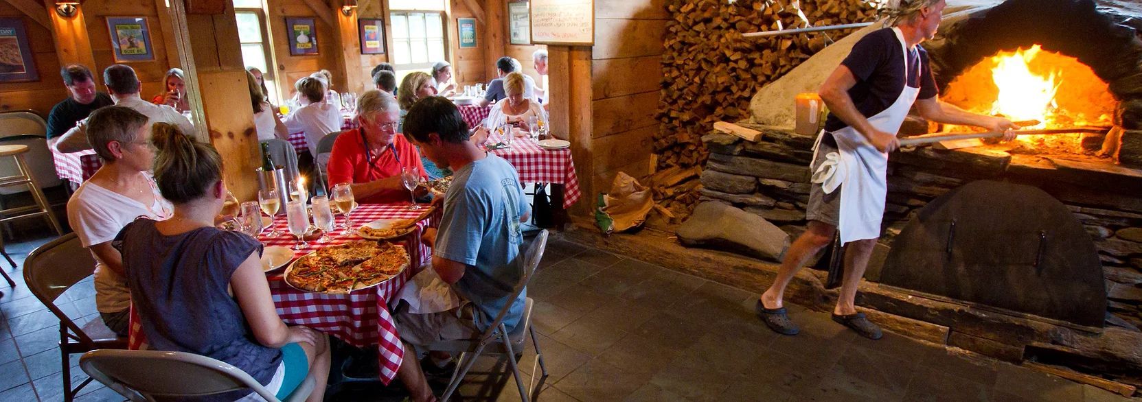 A group of people are sitting at tables in a restaurant eating pizza.