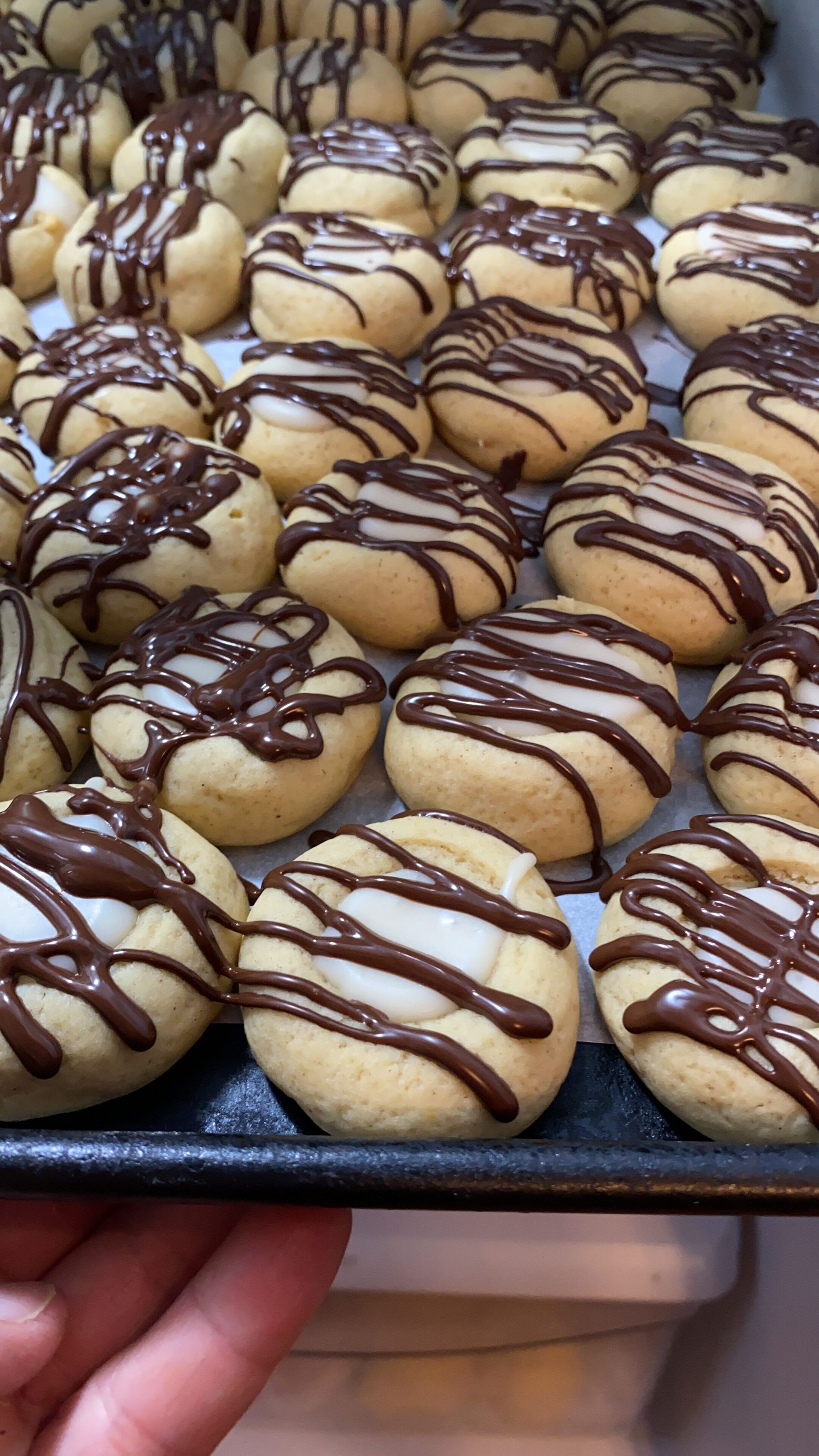 A person is holding a tray of cookies with chocolate icing on them.