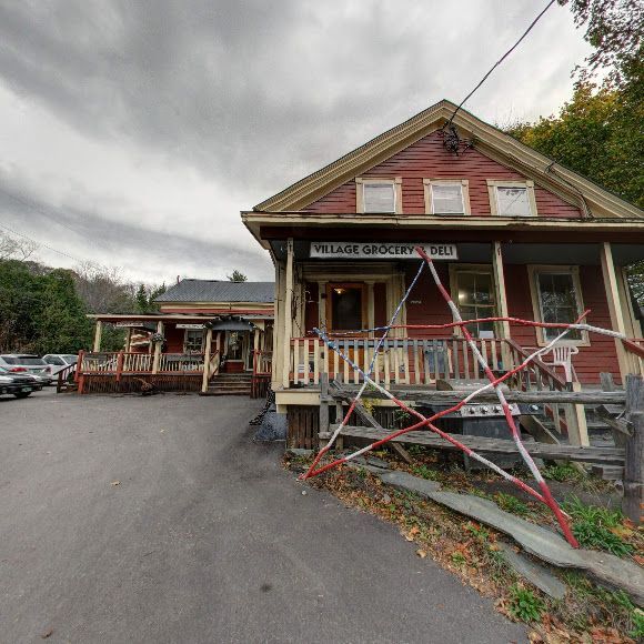 A red house with a porch and a sign that says village grocery deli