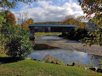 A covered bridge over a river surrounded by trees and grass.
