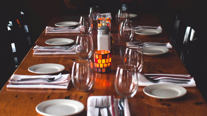 A long wooden table with plates , glasses , silverware and a candle.