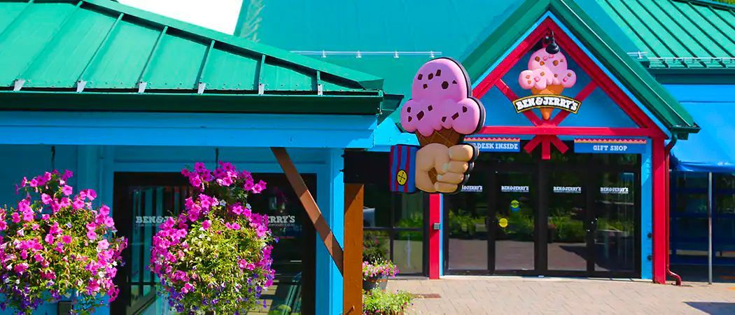 A person is holding an ice cream cone in front of an ice cream shop.