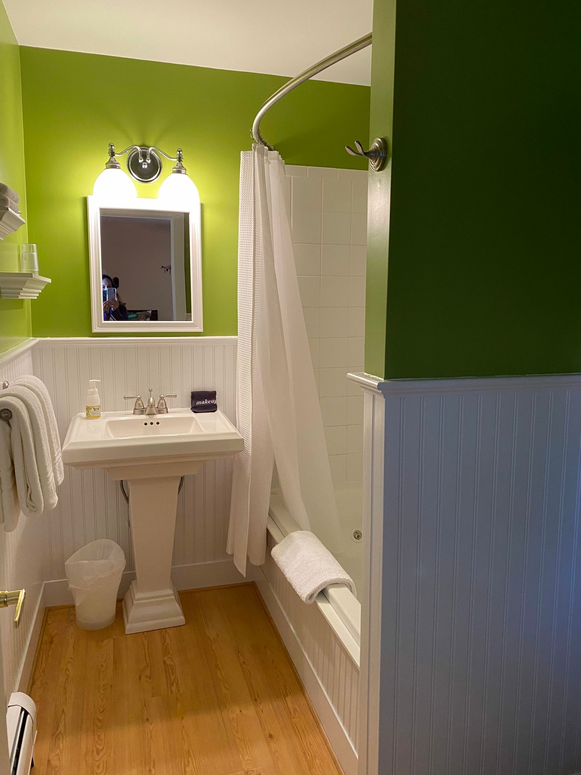 A bathroom with green walls , a sink , a mirror and a bathtub.