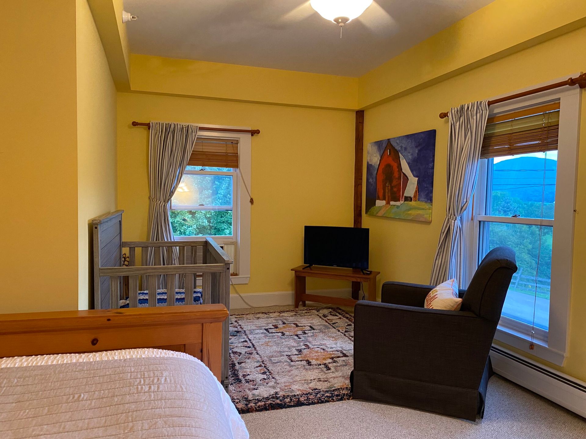 A bedroom with a crib , chair , and television.