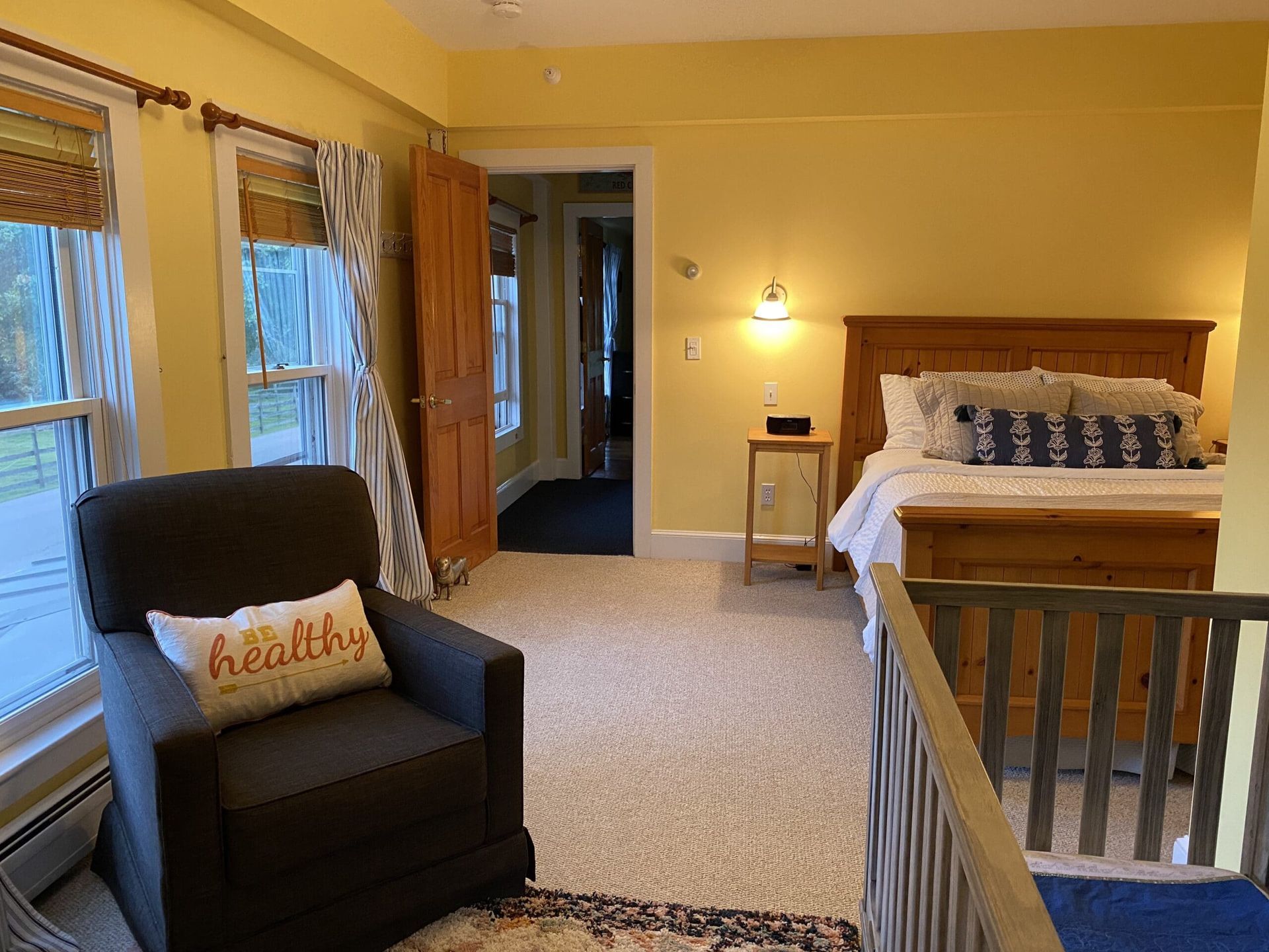 A bedroom with a bed , chair , and crib . the chair has a pillow that says healthy on it.