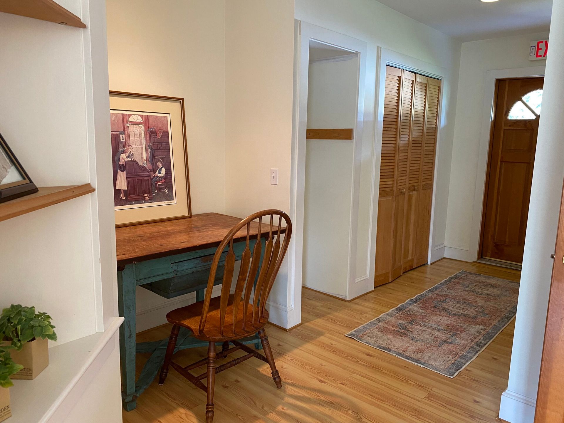 A hallway with a desk and chair in it and a picture on the wall.