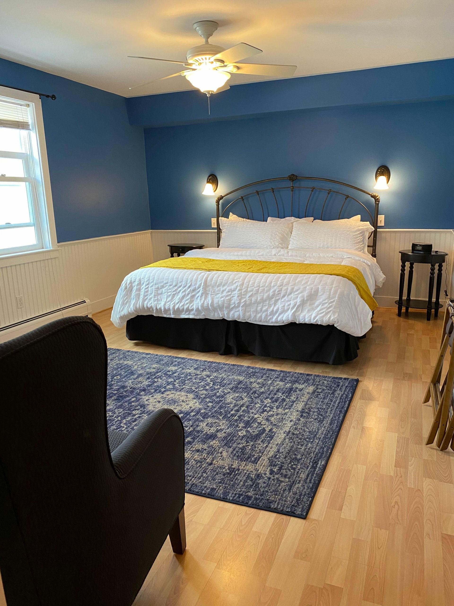 A bedroom with a large bed , chair , rug and ceiling fan.