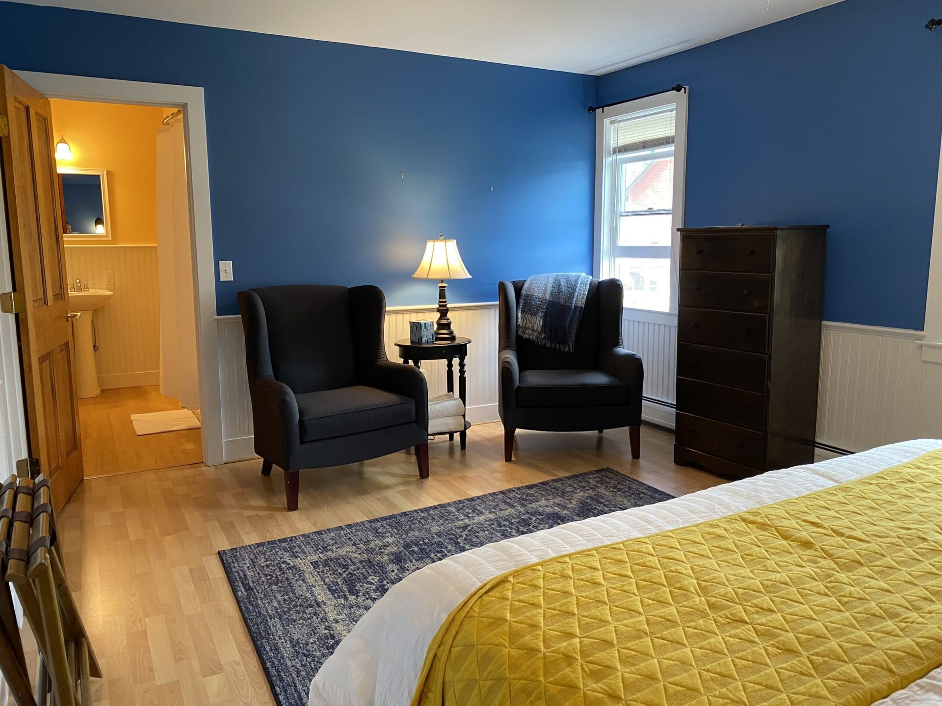 A bedroom with a bed , two chairs , a lamp and a dresser.