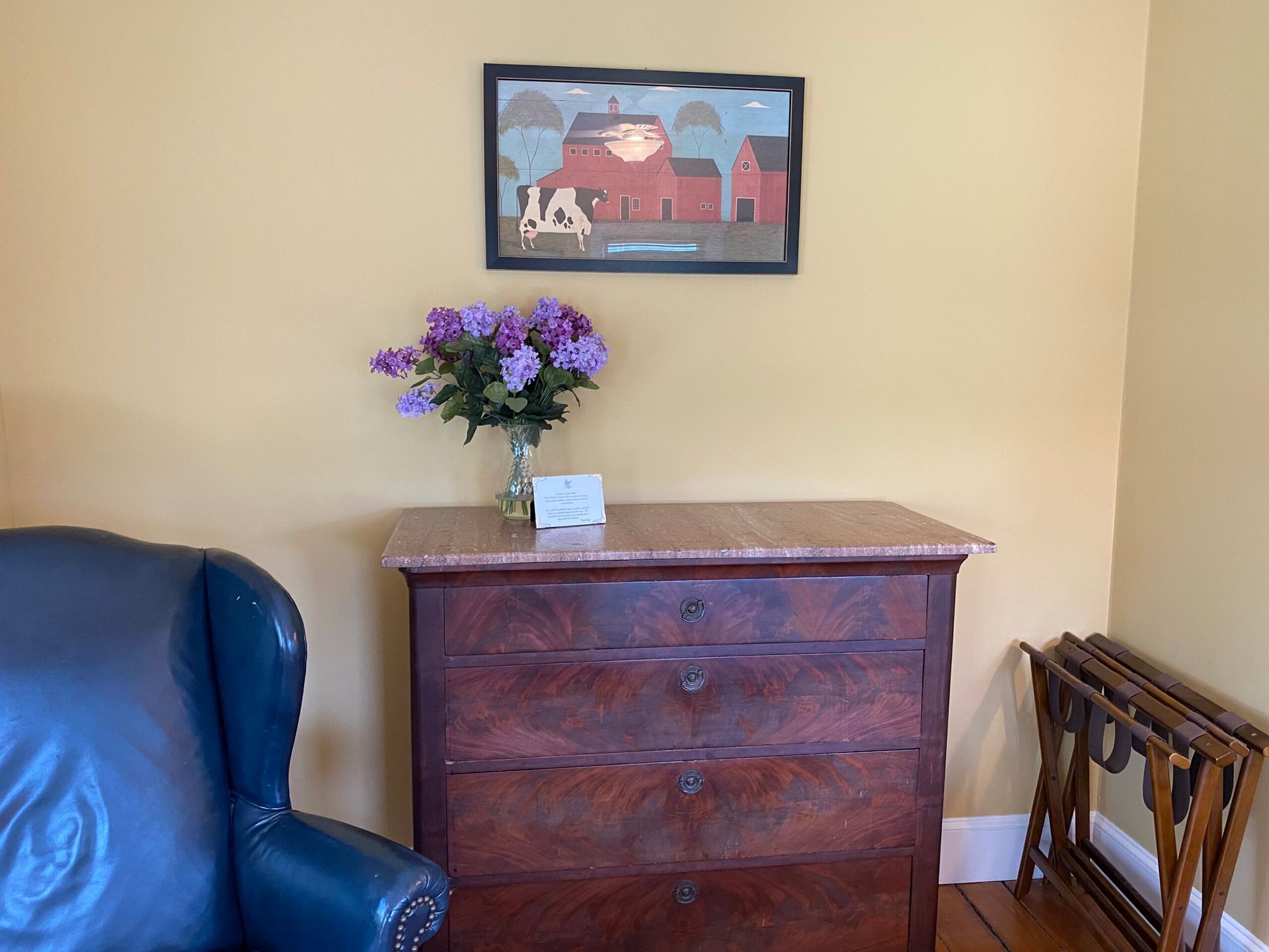 A room with a dresser and a chair and a picture on the wall above it