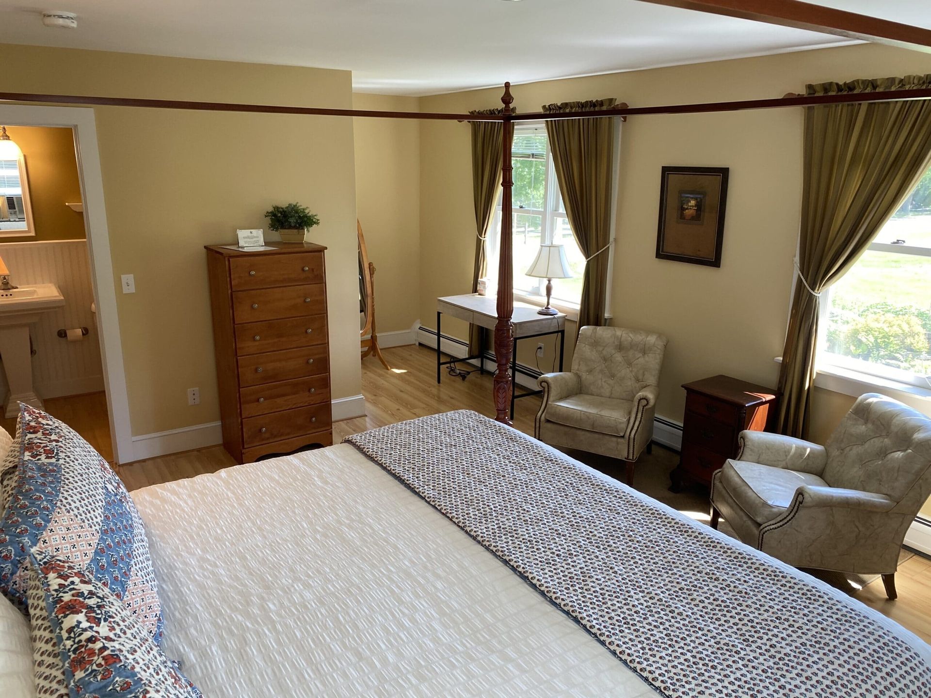 A bedroom with a four poster bed , chair , dresser and window.