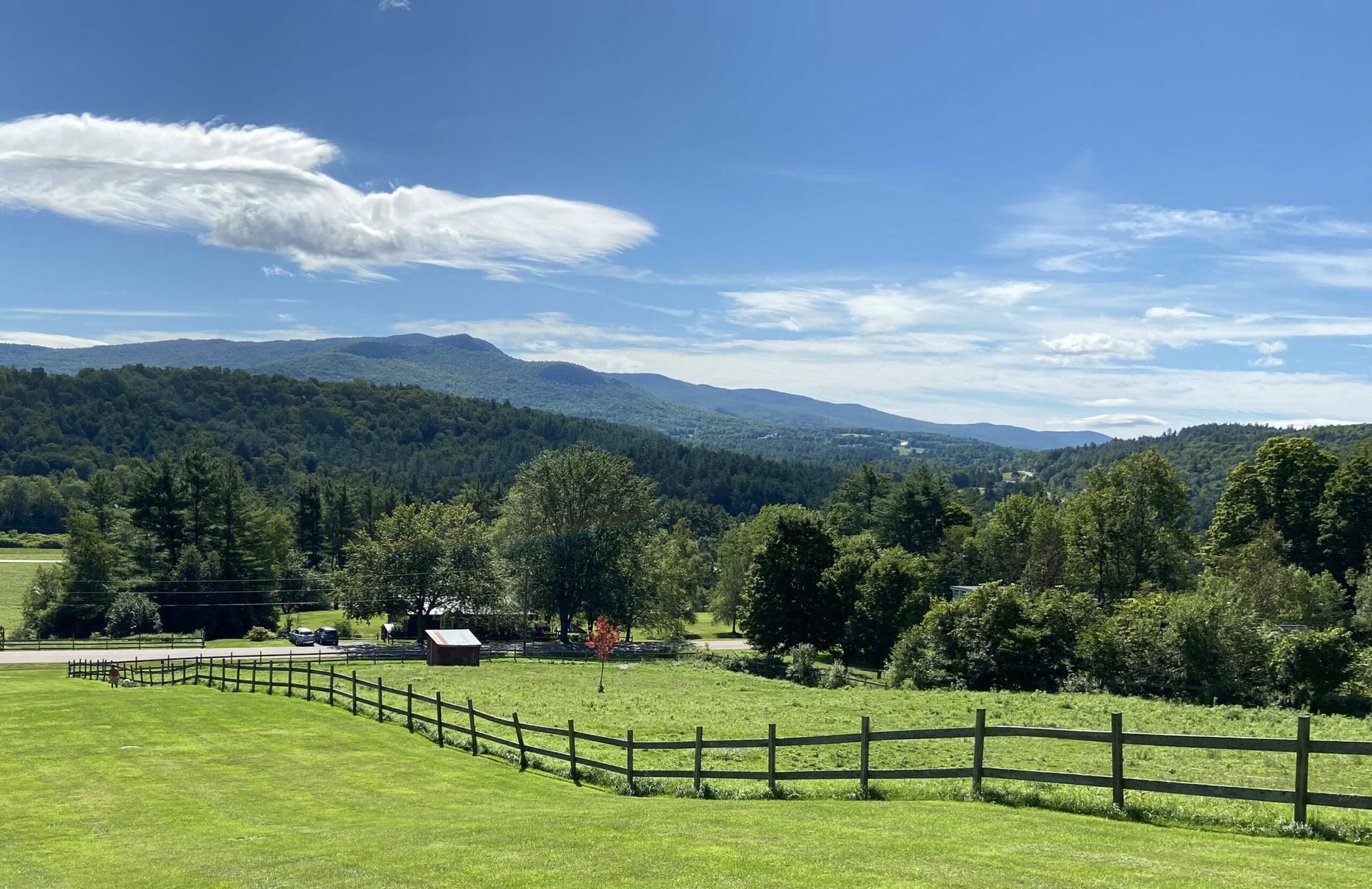 A wooden fence surrounds a grassy field with mountains in the background.