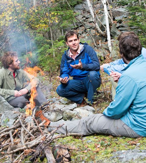 A group of men are sitting around a fire in the woods