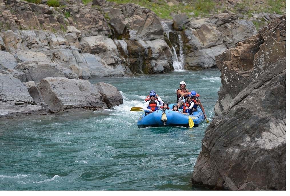 A group of people are rafting down a river near a waterfall.