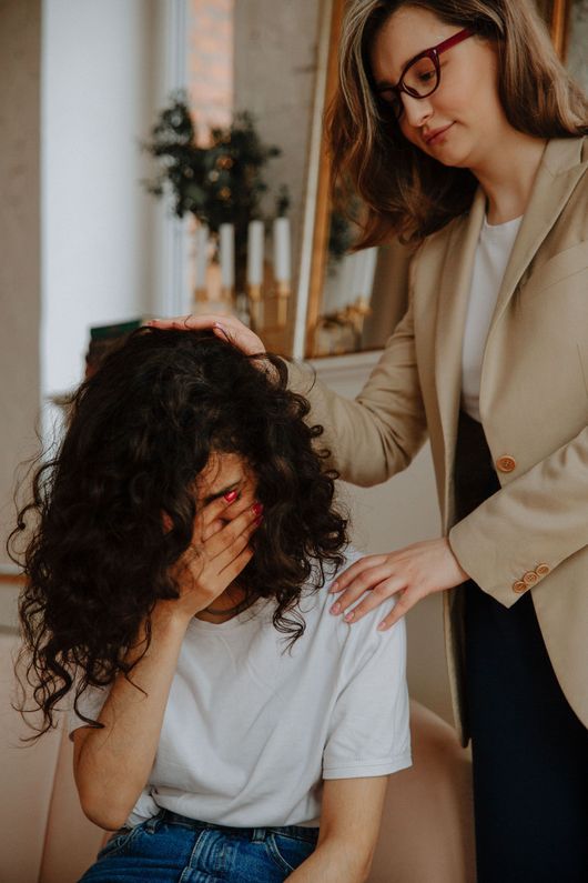 Woman comforting seated person with curly hair in a bright indoor room