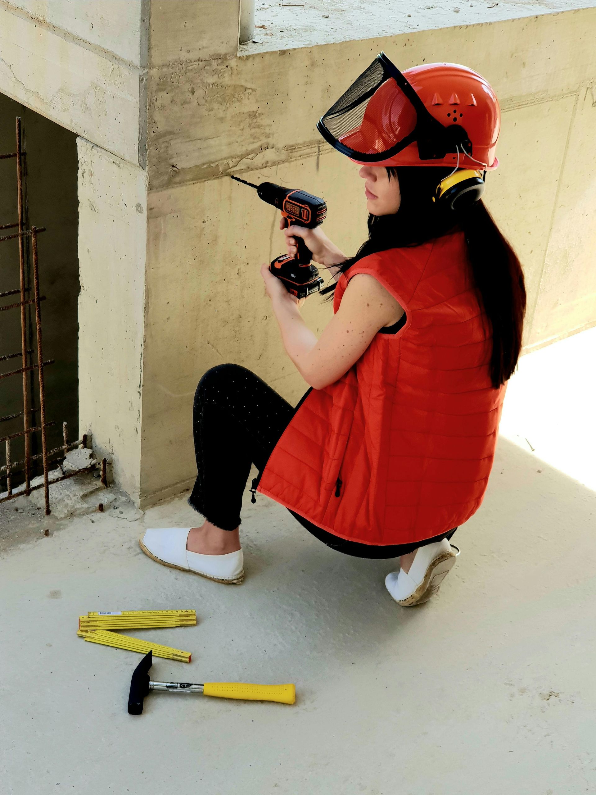 A woman wearing a red vest and a hard hat is using a drill