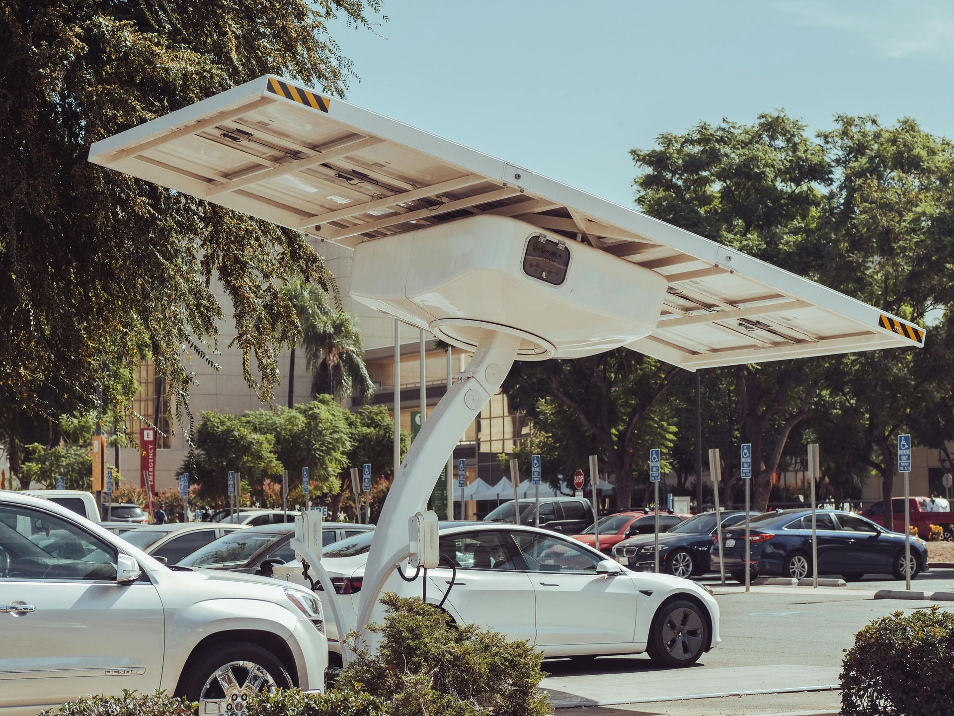 A white car is being charged by a solar panel in a parking lot.